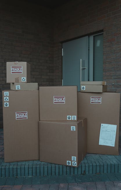Close-up image of a cardboard moving box labeled with black and blue marker, showing categories such as 'Name', 'Contents', 'Order No.', and 'Room', with 'KITCHEN' written in blue under the 'Room' sec